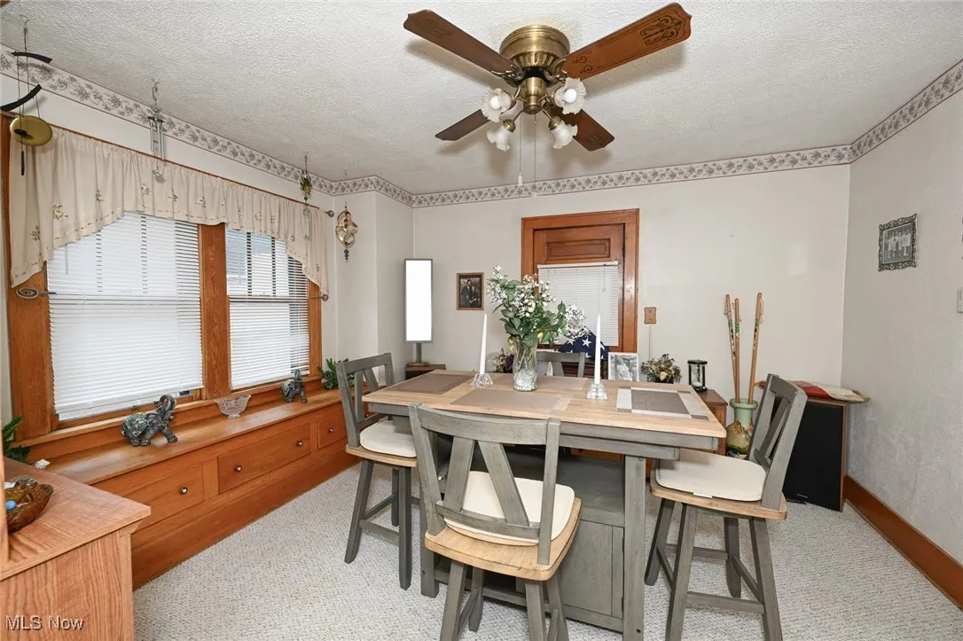 Dining area featuring a ceiling fan, light carpet, and a textured ceiling