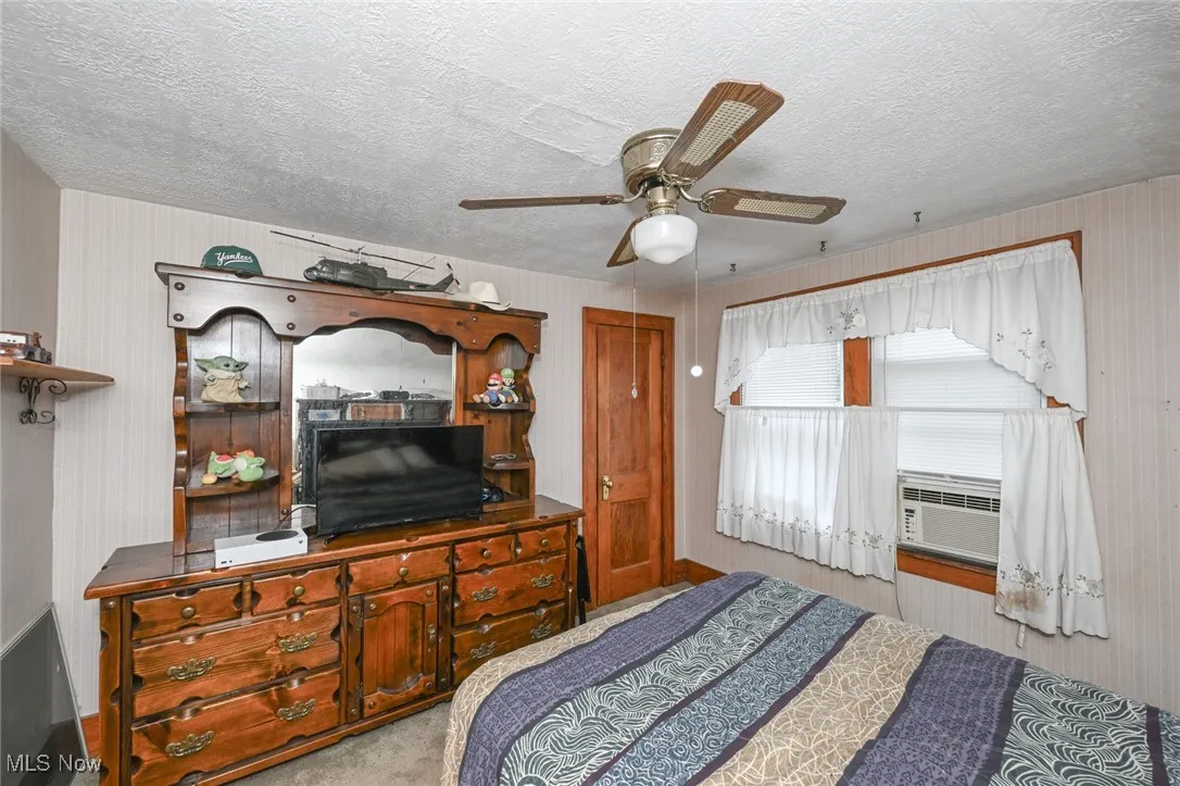 Carpeted bedroom featuring cooling unit, a textured ceiling, and a ceiling fan