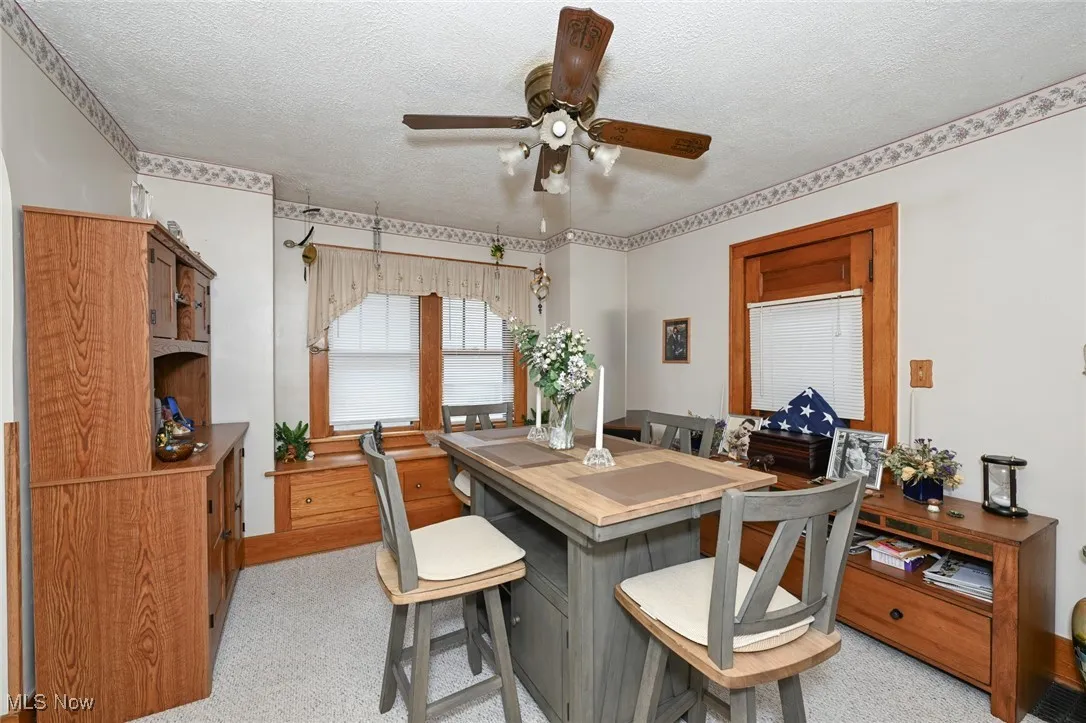 Dining room with ceiling fan, a textured ceiling, and light carpet