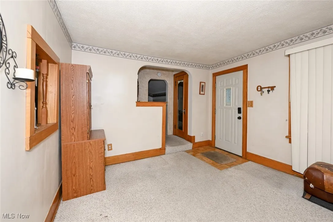 Carpeted foyer entrance featuring a textured ceiling and arched walkways