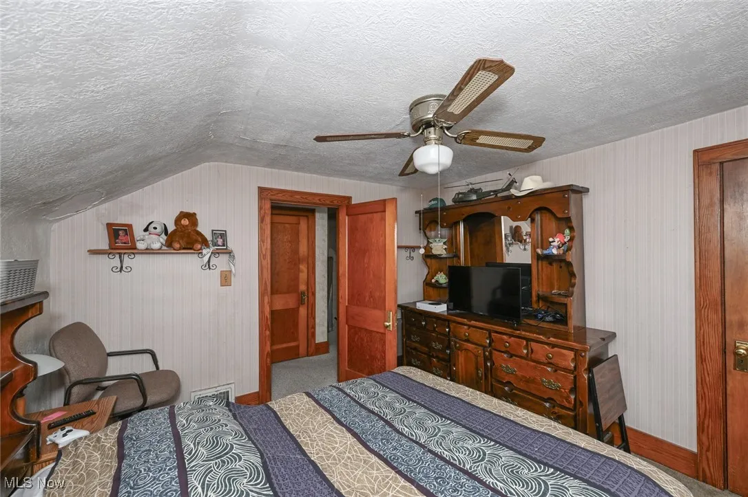 Carpeted bedroom with a textured ceiling, lofted ceiling, and ceiling fan