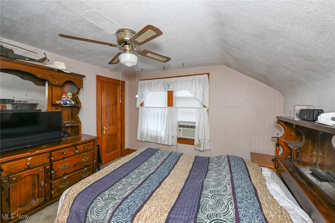 Bedroom with a textured ceiling, vaulted ceiling, ceiling fan, carpet floors, and cooling unit