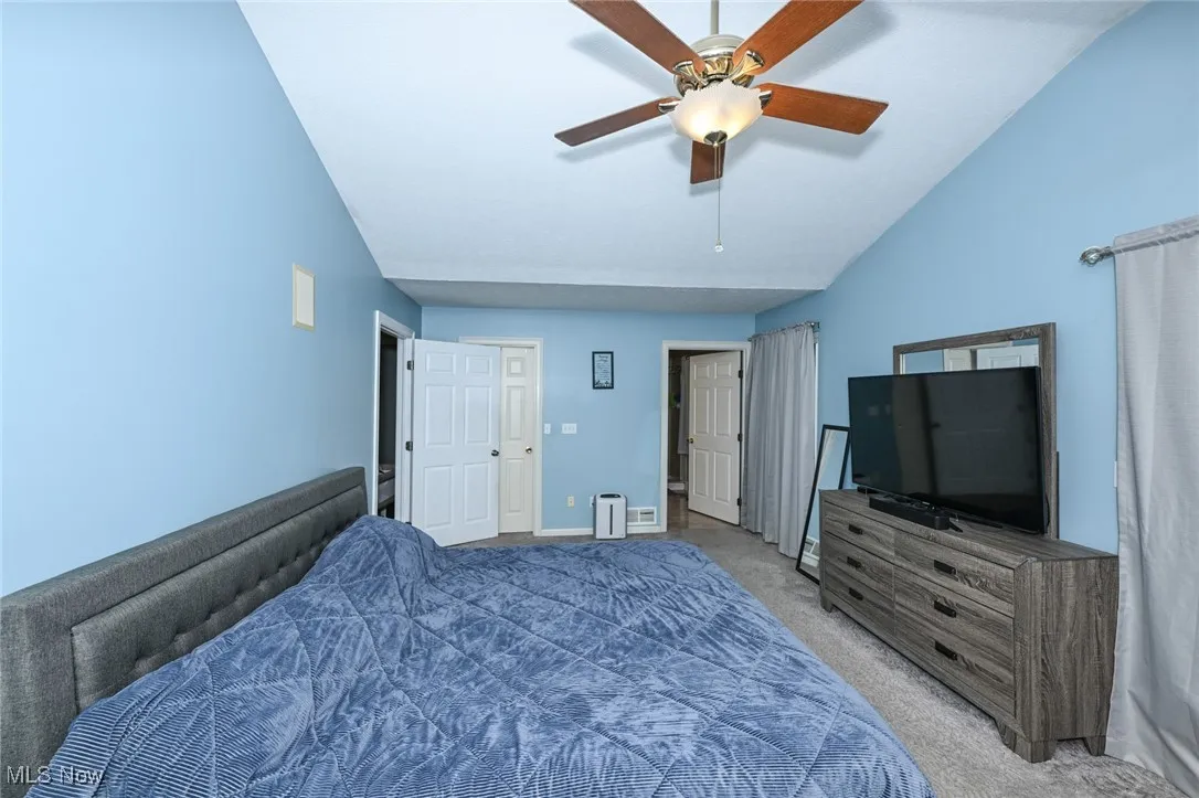 Bedroom featuring light colored carpet, vaulted ceiling, and a ceiling fan