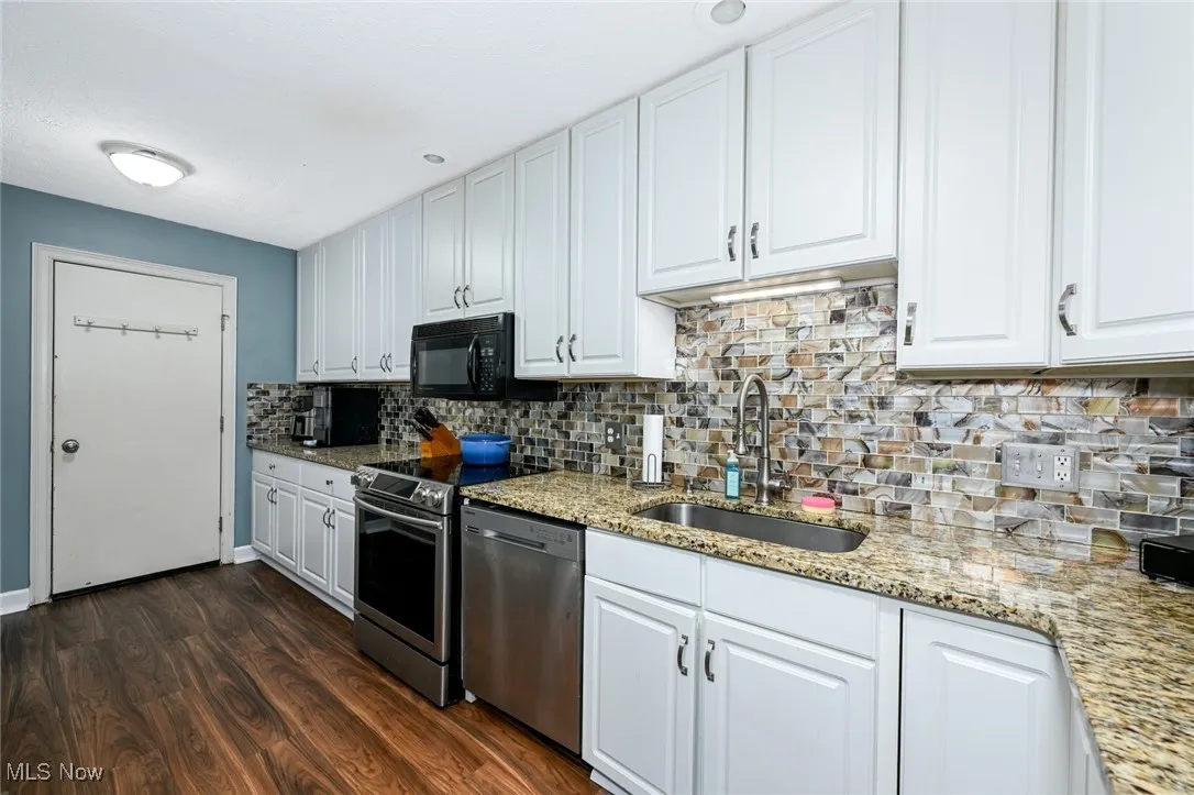 Kitchen with stainless steel appliances, white cabinets, backsplash, dark wood-style floors, and light stone counters