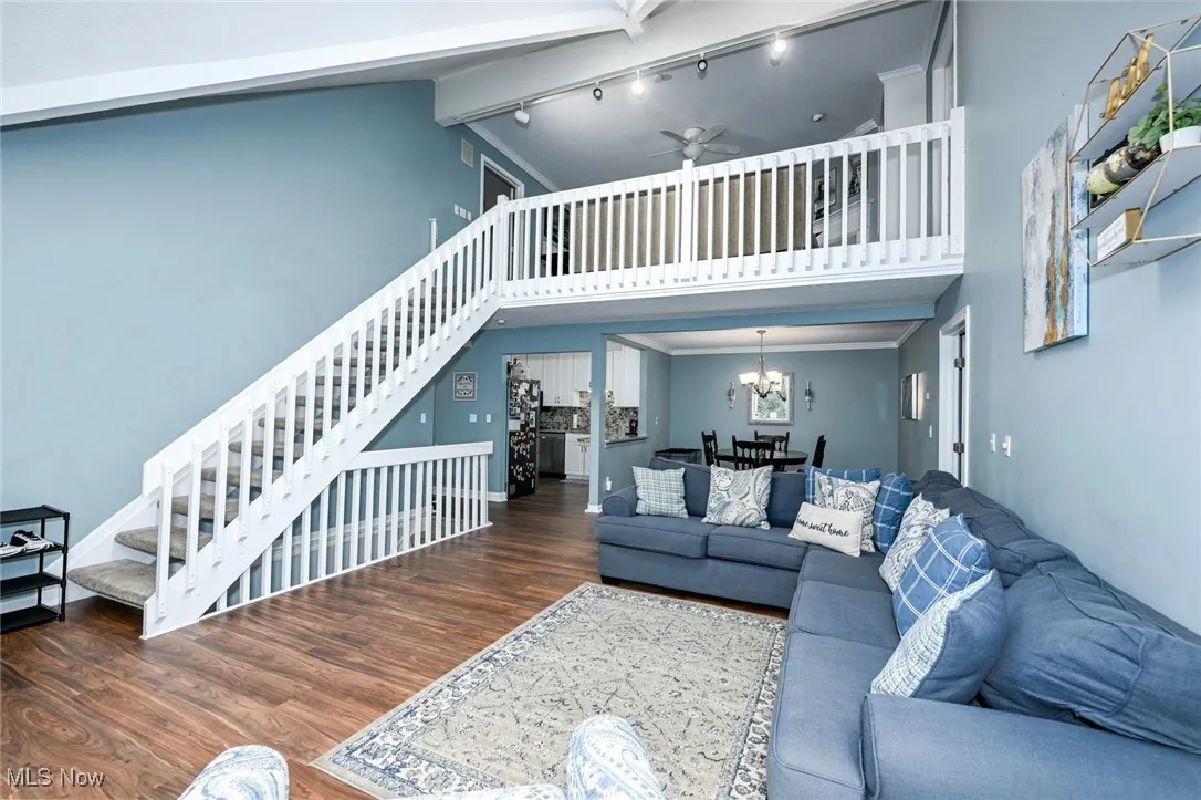 Living room featuring high vaulted ceiling, wood finished floors, stairway, a chandelier, and a ceiling fan