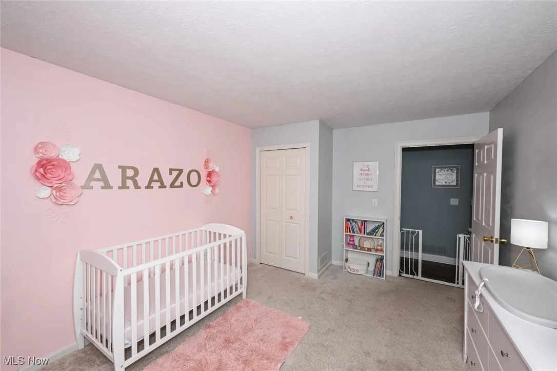 Bedroom featuring light colored carpet, a nursery area, a textured ceiling, and a closet