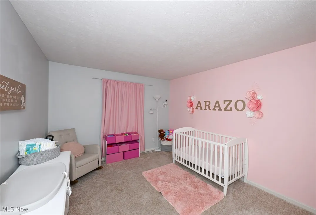 Carpeted bedroom featuring a nursery area and a textured ceiling