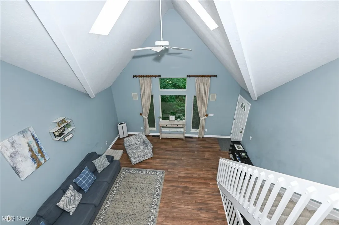 Living room featuring a skylight, wood finished floors, ceiling fan, and high vaulted ceiling