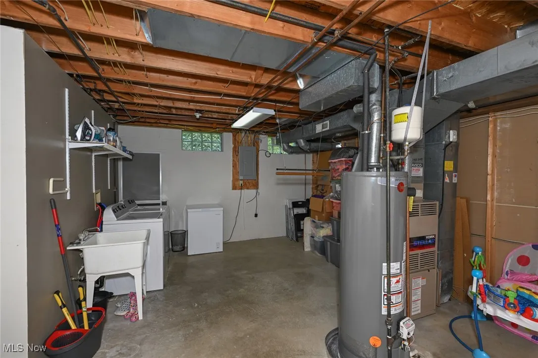Below grade area featuring gas water heater, washer and clothes dryer, electric panel, and refrigerator
