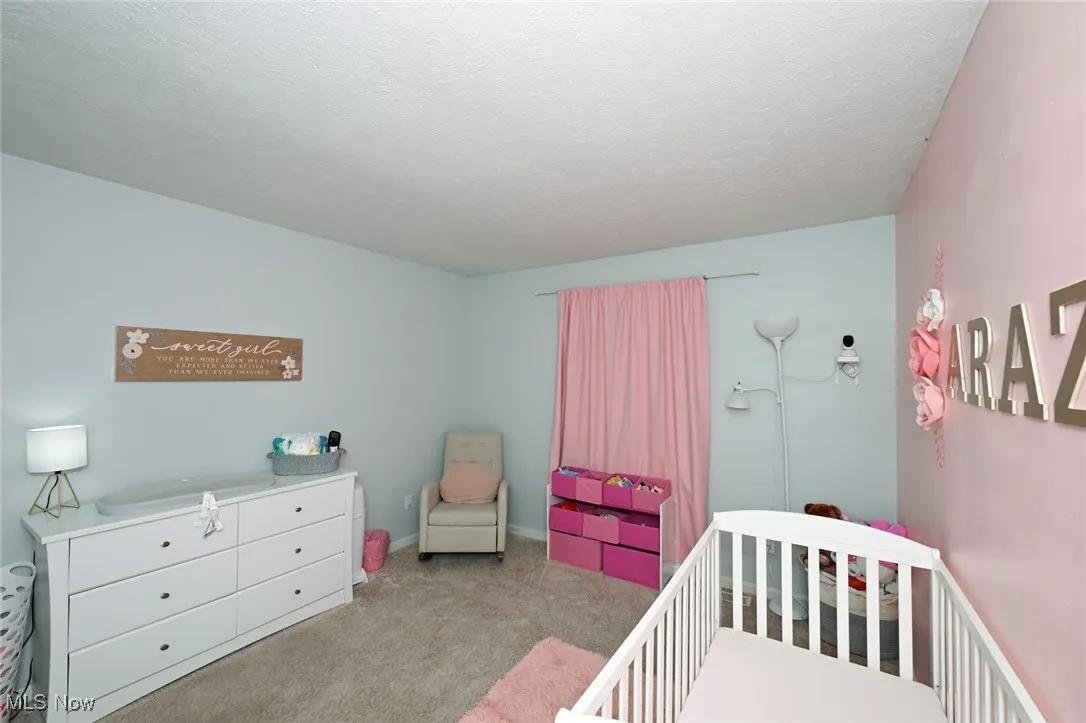 Carpeted bedroom featuring a nursery area and a textured ceiling