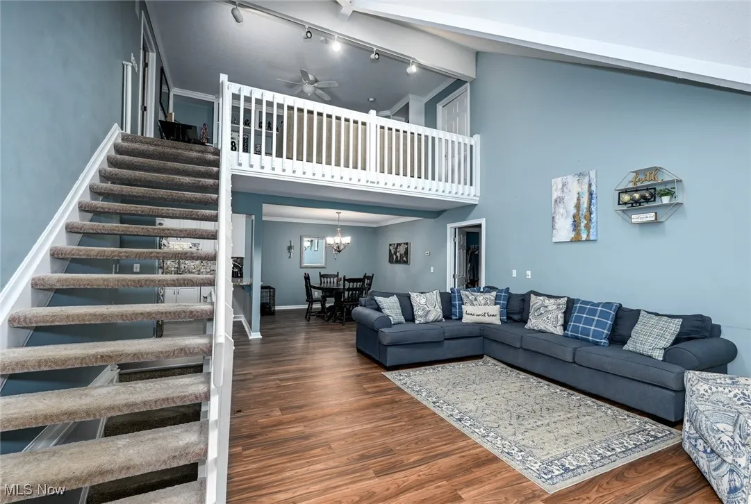 Living area with wood finished floors, high vaulted ceiling, stairs, a chandelier, and a ceiling fan