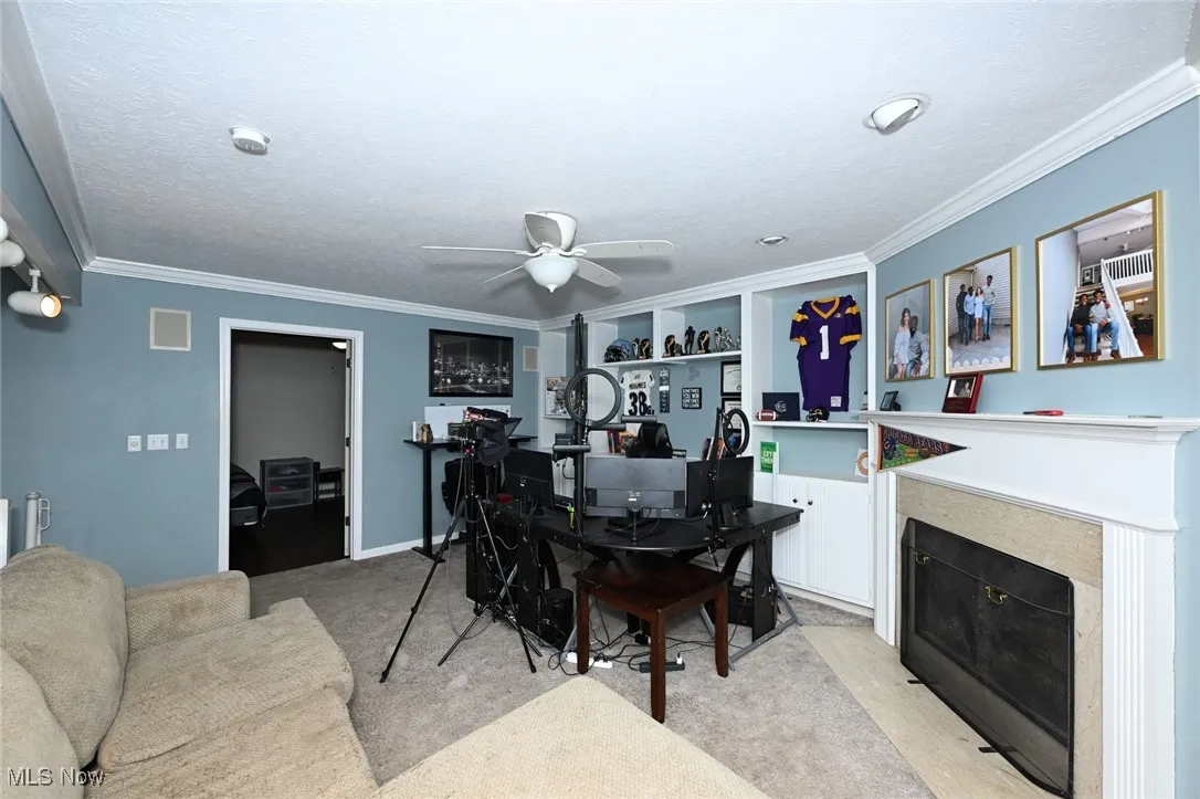 Dining area featuring light colored carpet, a fireplace with flush hearth, a ceiling fan, a desk, and ornamental molding