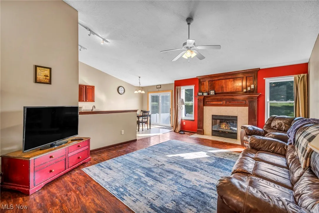 Living room with ceiling fan, lofted ceiling, dark wood-type flooring, a textured ceiling, and a tiled fireplace