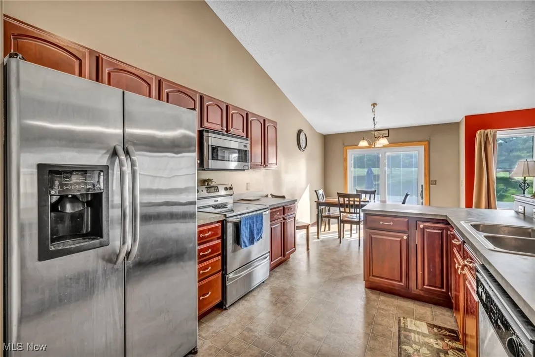 Kitchen featuring appliances with stainless steel finishes, lofted ceiling, a textured ceiling, and decorative light fixtures