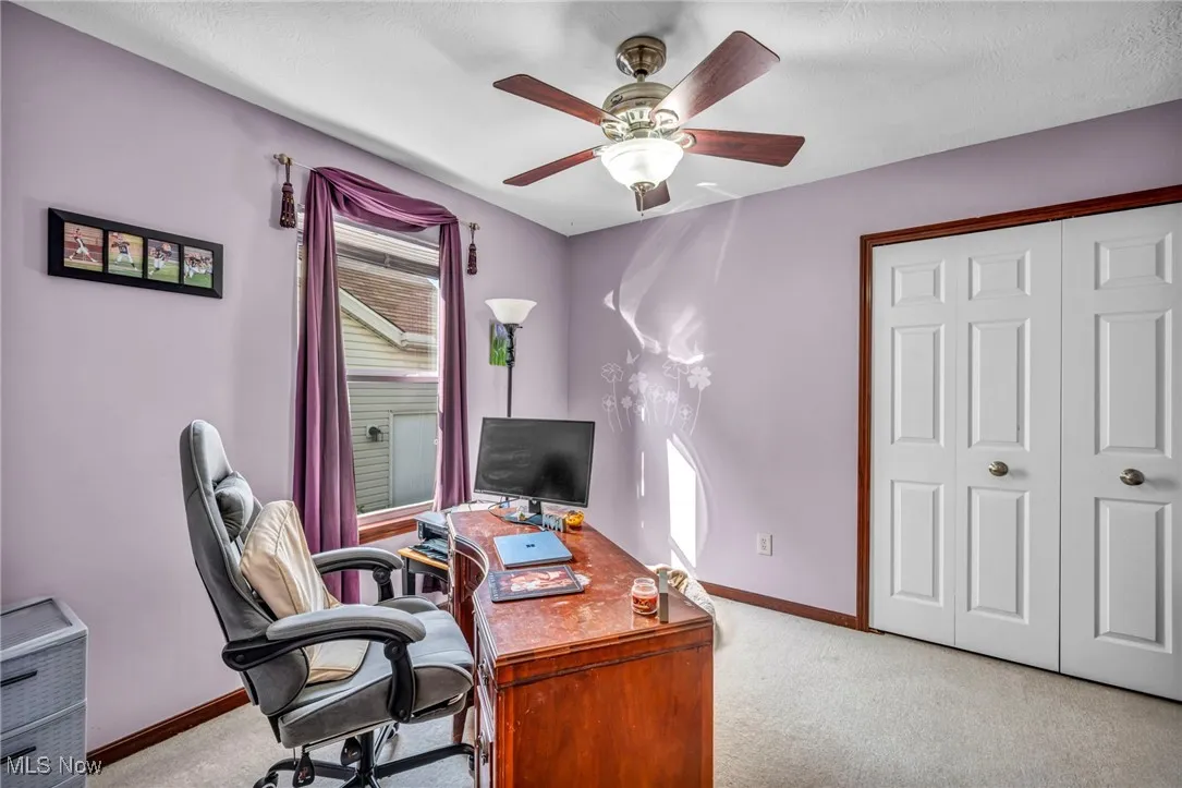Carpeted home office with a ceiling fan and baseboards