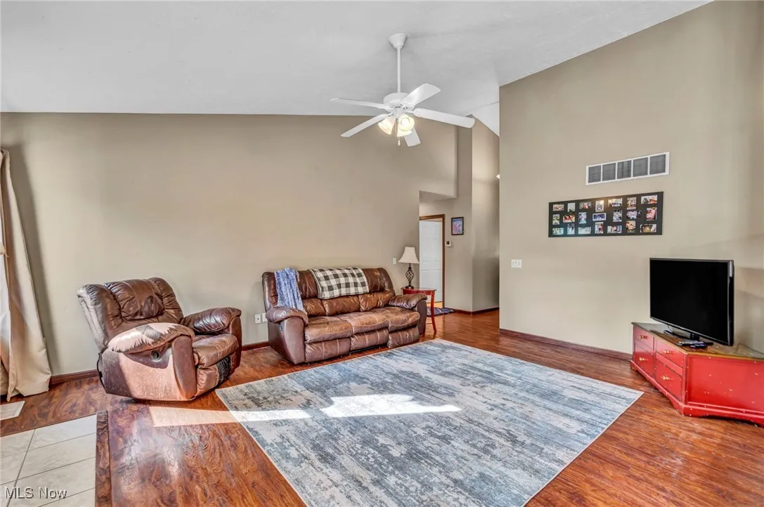 Living area with ceiling fan, wood finished floors, and high vaulted ceiling