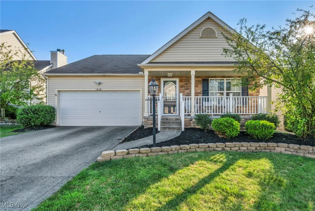 Single story home with covered porch, a garage, driveway, stone siding, and a front yard