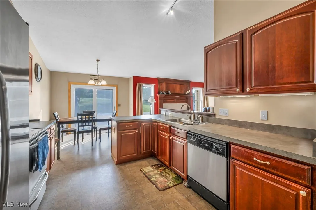 Kitchen with stainless steel appliances, a peninsula, a chandelier, pendant lighting, and light floors