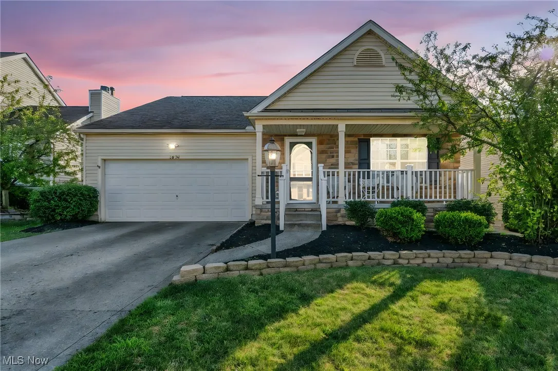 Ranch-style home featuring covered porch, driveway, an attached garage, a front lawn, and stone siding