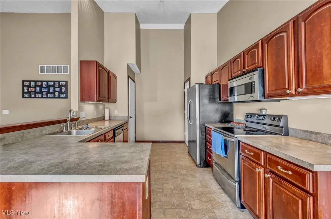 Kitchen featuring appliances with stainless steel finishes, a towering ceiling, and a peninsula