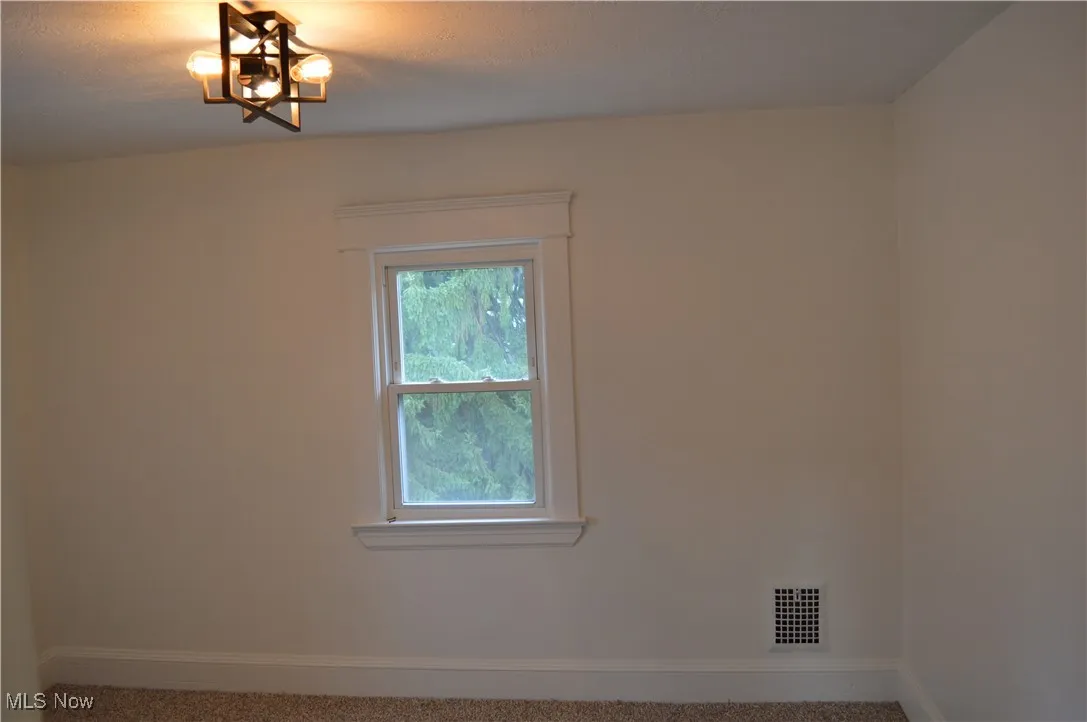 Carpeted spare room featuring baseboards and a chandelier