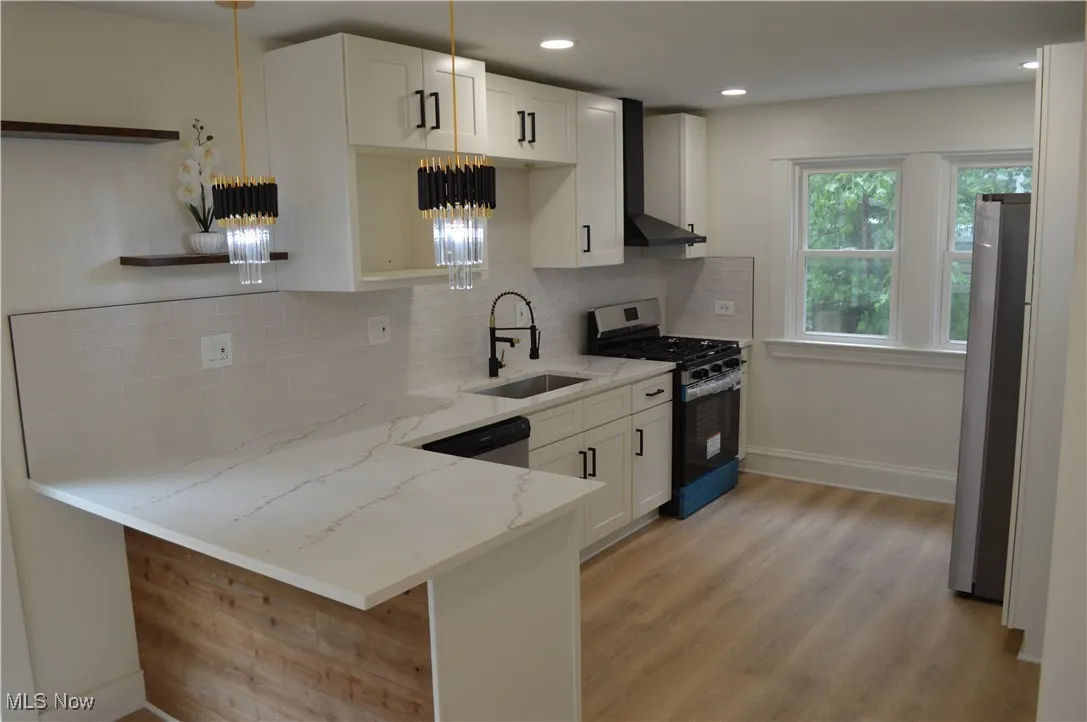 Kitchen featuring stainless steel appliances, wall chimney range hood, light stone countertops, light wood-type flooring, and decorative backsplash