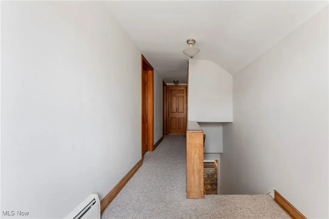 Corridor featuring carpet flooring, a baseboard radiator, and vaulted ceiling