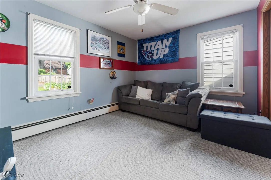 Carpeted living area with baseboard heating and ceiling fan