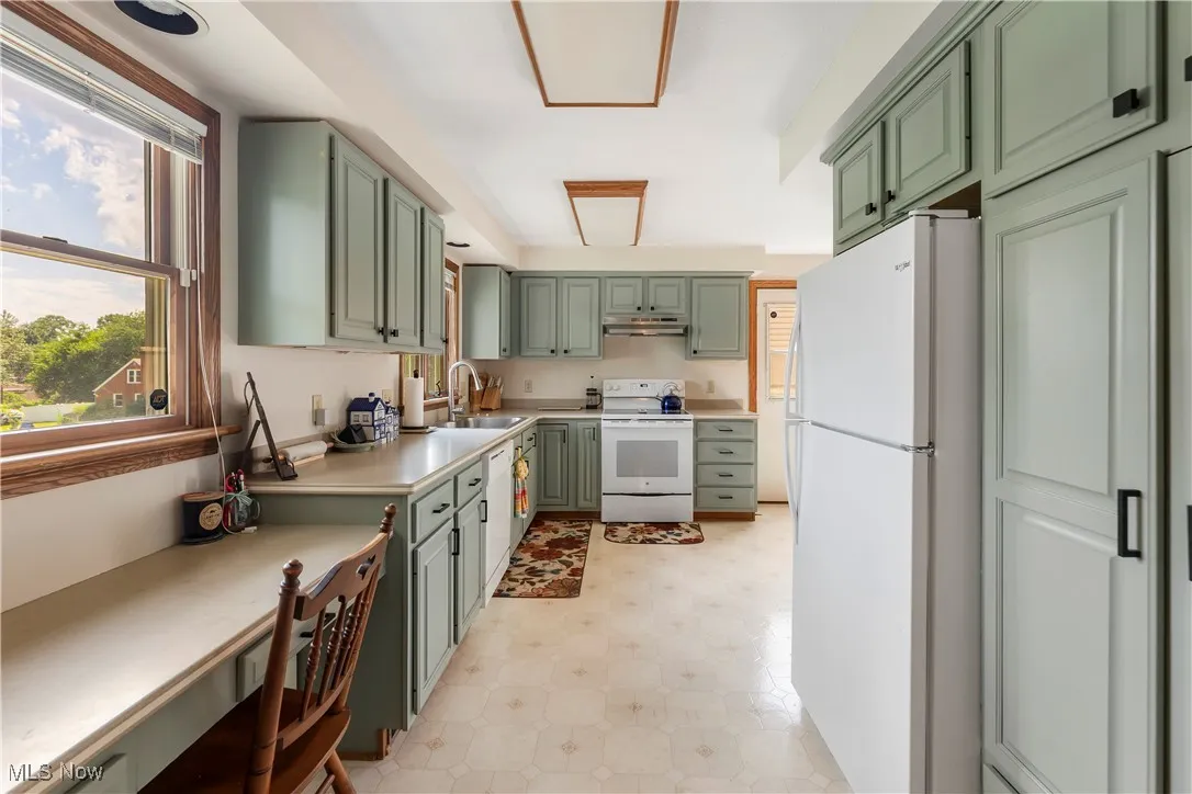Kitchen with green cabinetry, white appliances, under cabinet range hood, and plenty of natural light
