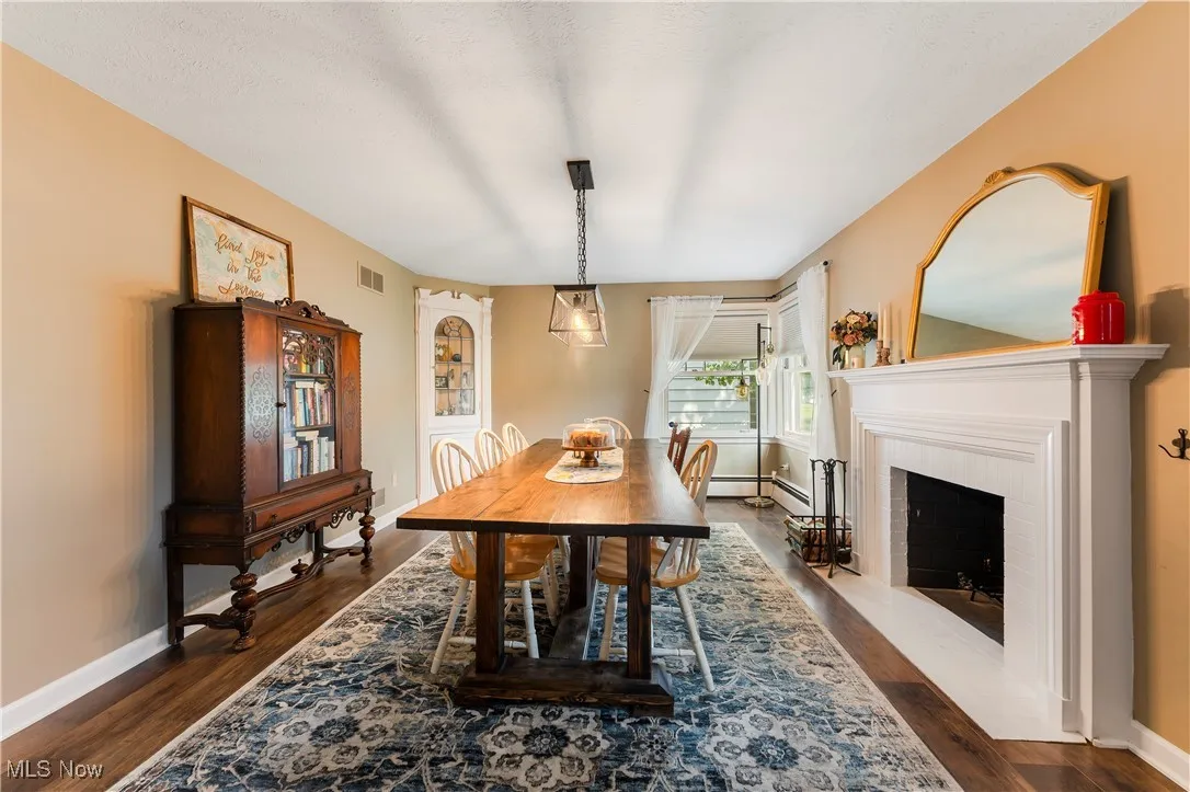 Dining room featuring dark wood-style floors, a fireplace with flush hearth, and a baseboard radiator