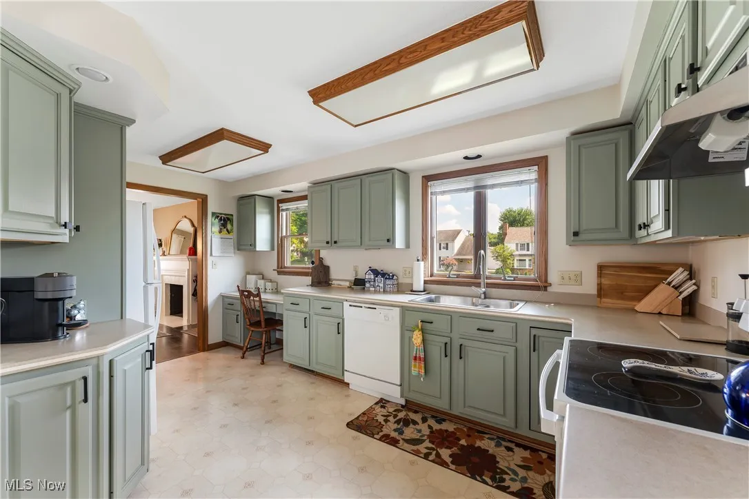 Kitchen featuring green cabinets, white appliances, under cabinet range hood, light floors, and light countertops