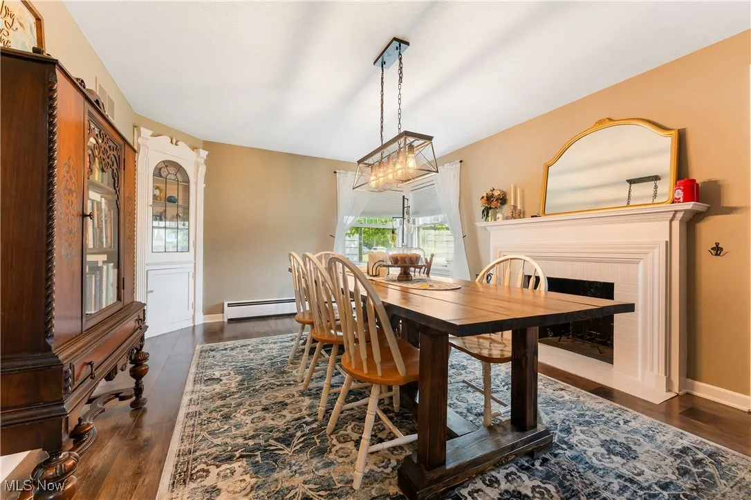 Dining room featuring baseboard heating, dark wood-style floors, and a fireplace with flush hearth