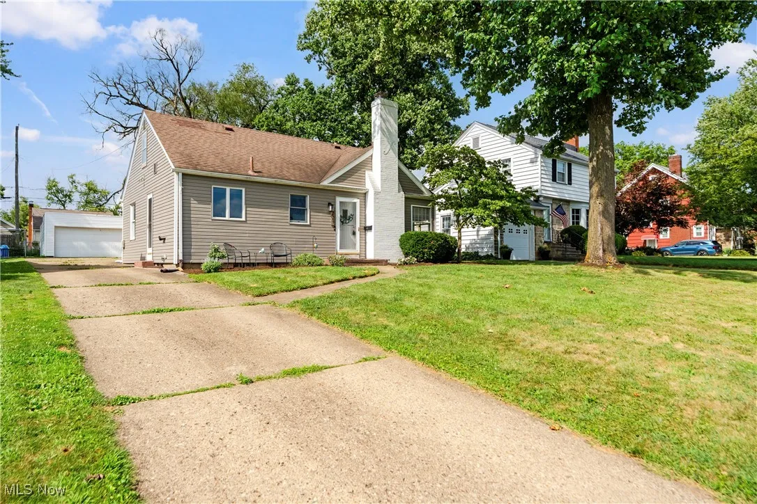 View of front of home with a chimney, a front lawn, an outbuilding, and a detached garage