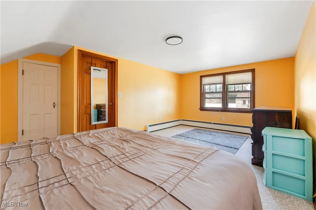 Carpeted bedroom with a baseboard heating unit and lofted ceiling