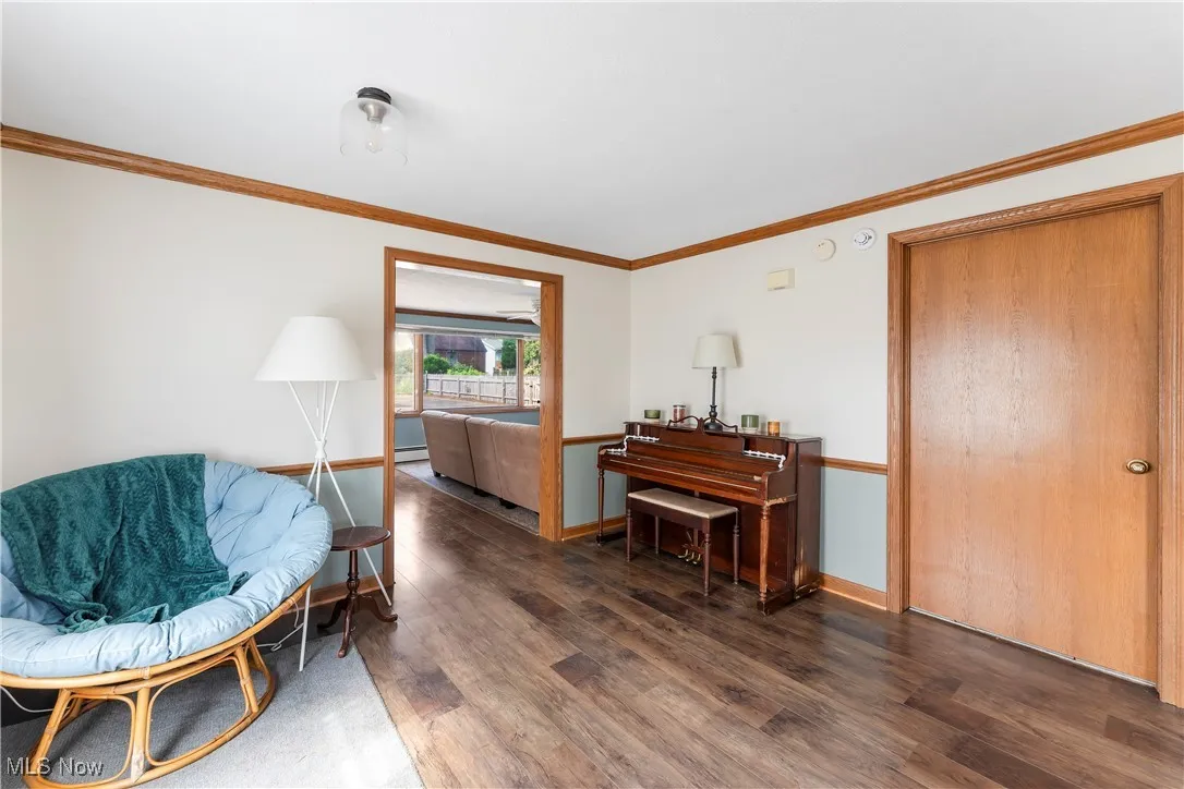 Sitting room with wood finished floors, ornamental molding, and a baseboard heating unit