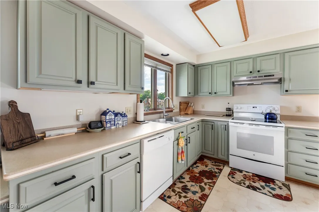 Kitchen featuring white appliances, under cabinet range hood, green cabinets, and light countertops