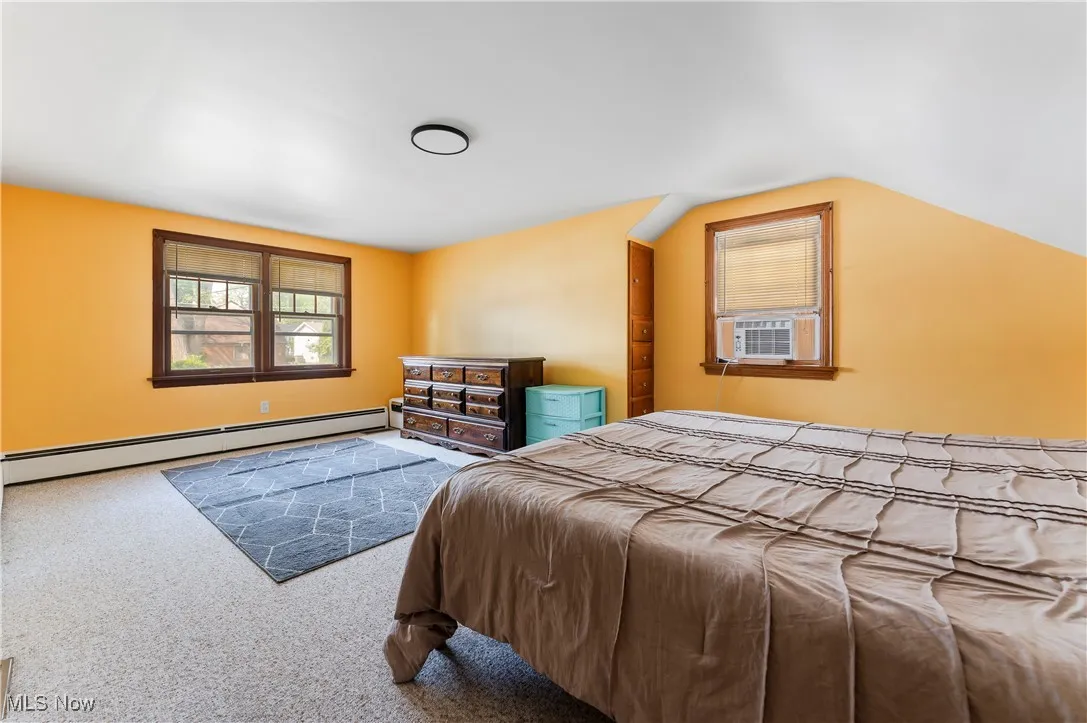 Carpeted bedroom featuring baseboard heating, cooling unit, and lofted ceiling