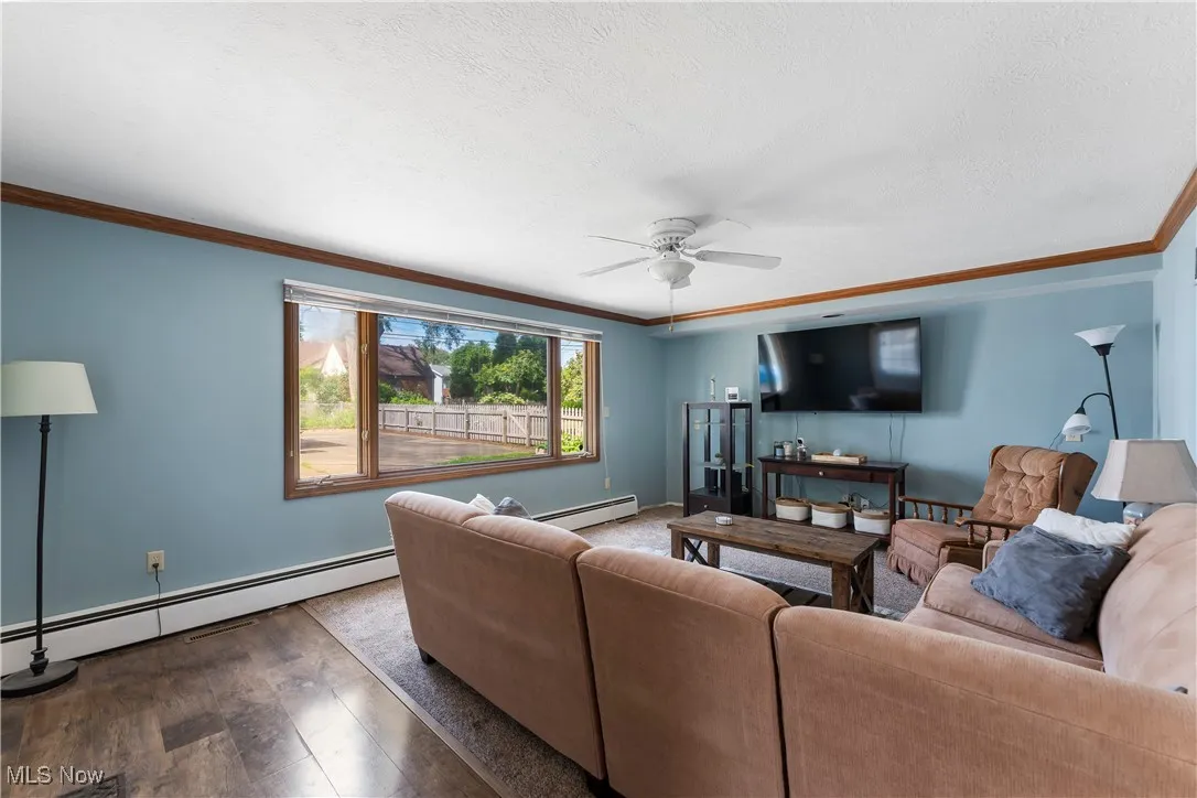 Living area featuring a baseboard radiator, ceiling fan, hardwood / wood-style flooring, and ornamental molding
