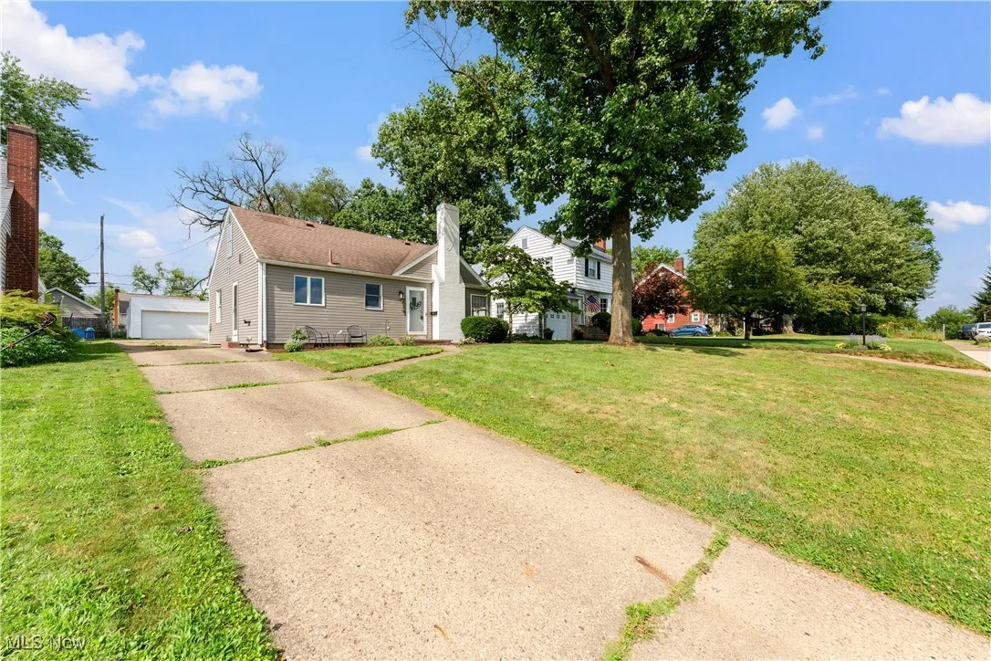 View of front of house with a chimney, a front lawn, a detached garage, and a shingled roof
