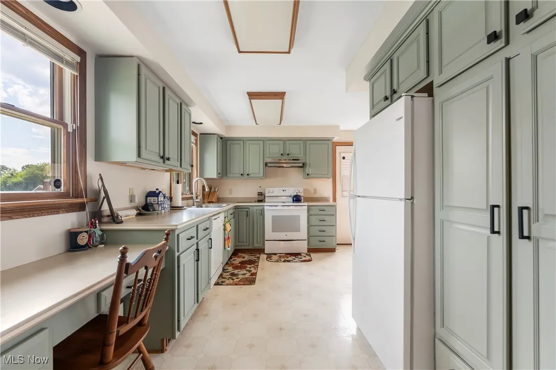 Kitchen featuring green cabinets, white appliances, under cabinet range hood, and light floors