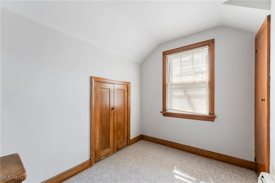 Unfurnished bedroom with a baseboard heating unit, vaulted ceiling, and light colored carpet