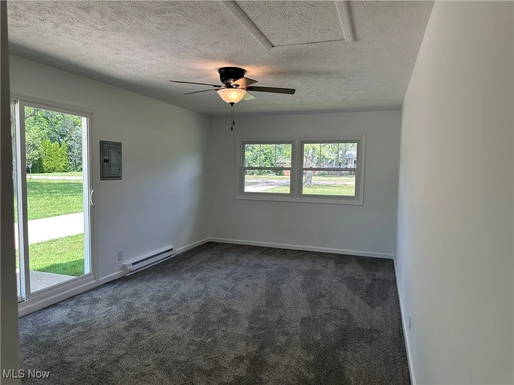 Unfurnished room with a baseboard heating unit, electric panel, dark carpet, healthy amount of natural light, and a textured ceiling