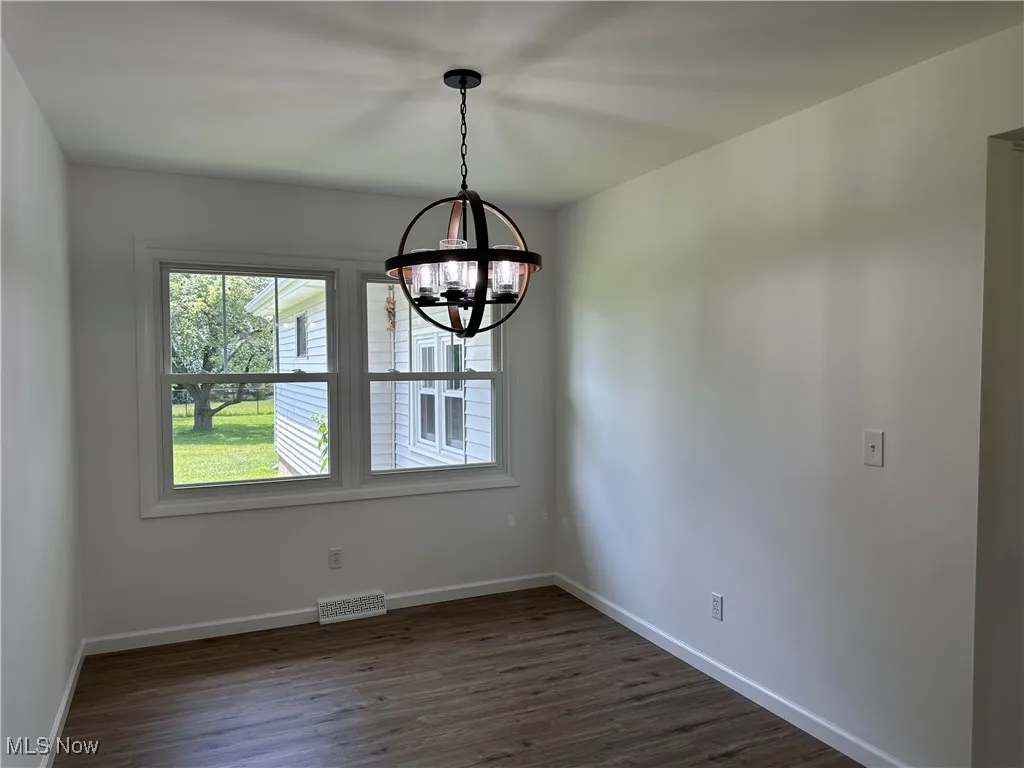 Empty room with a chandelier and dark wood finished floors
