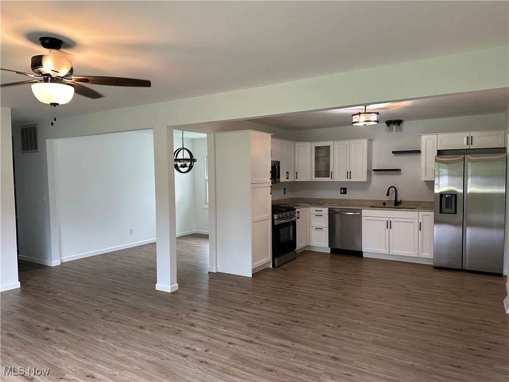 Kitchen featuring appliances with stainless steel finishes, dark wood finished floors, white cabinetry, a chandelier, and open floor plan