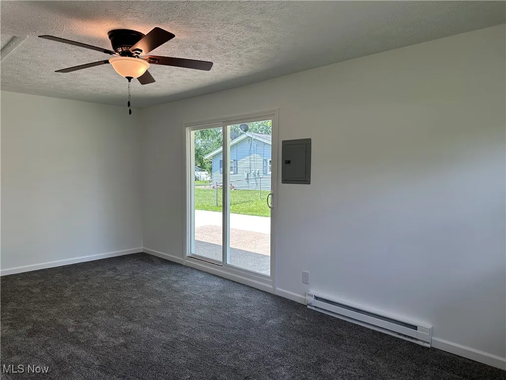 Spare room with a baseboard radiator, a textured ceiling, electric panel, dark colored carpet, and a ceiling fan