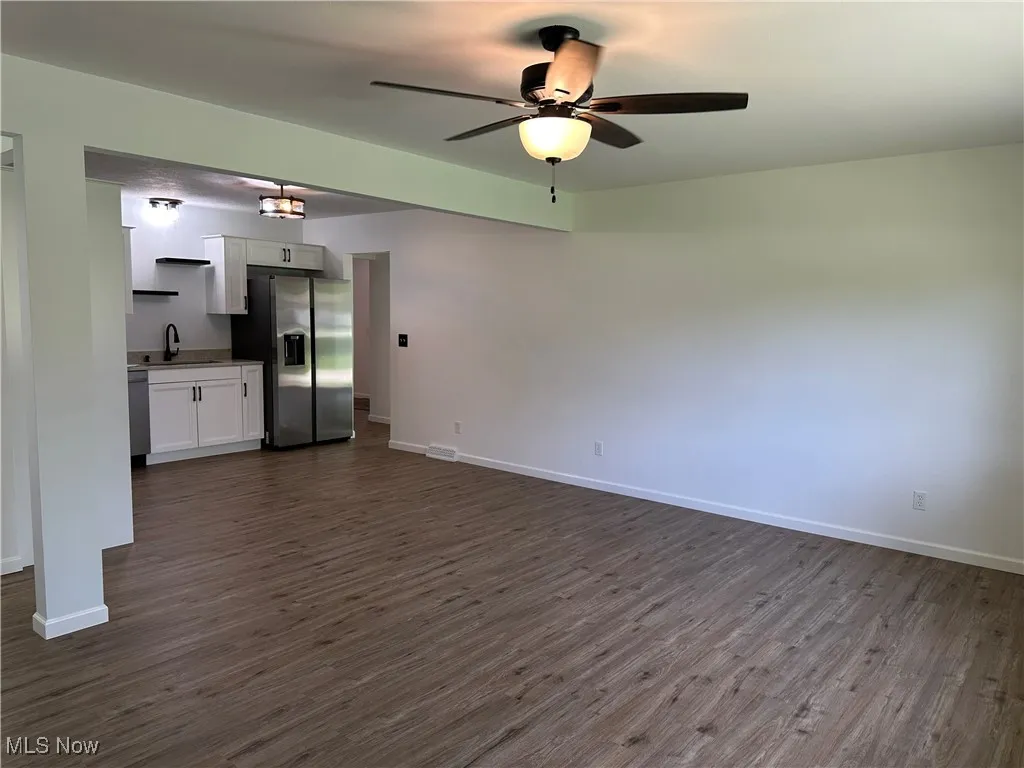 Unfurnished living room featuring dark wood-style flooring and ceiling fan