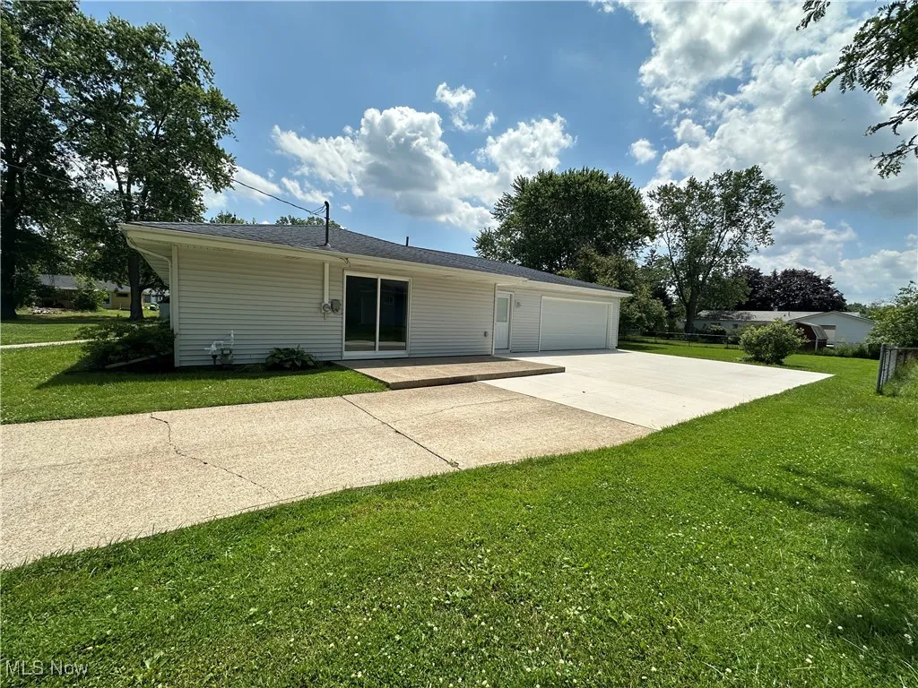 Rear view of property featuring concrete driveway, a lawn, a garage, and a patio area