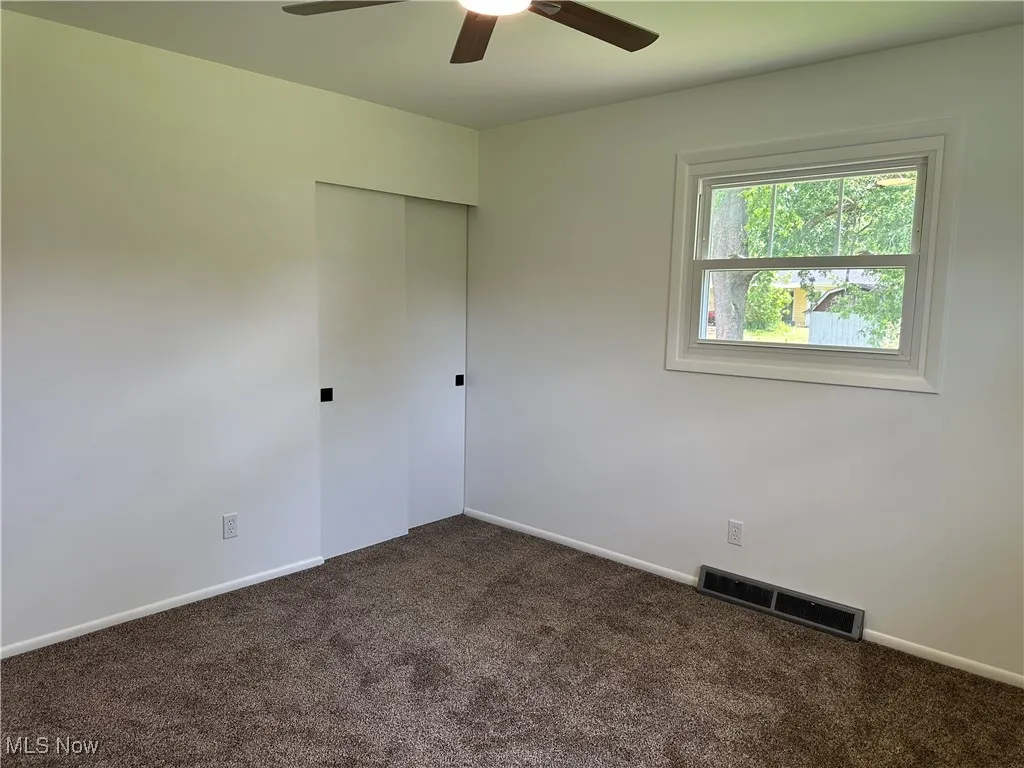 Unfurnished room featuring ceiling fan and dark colored carpet