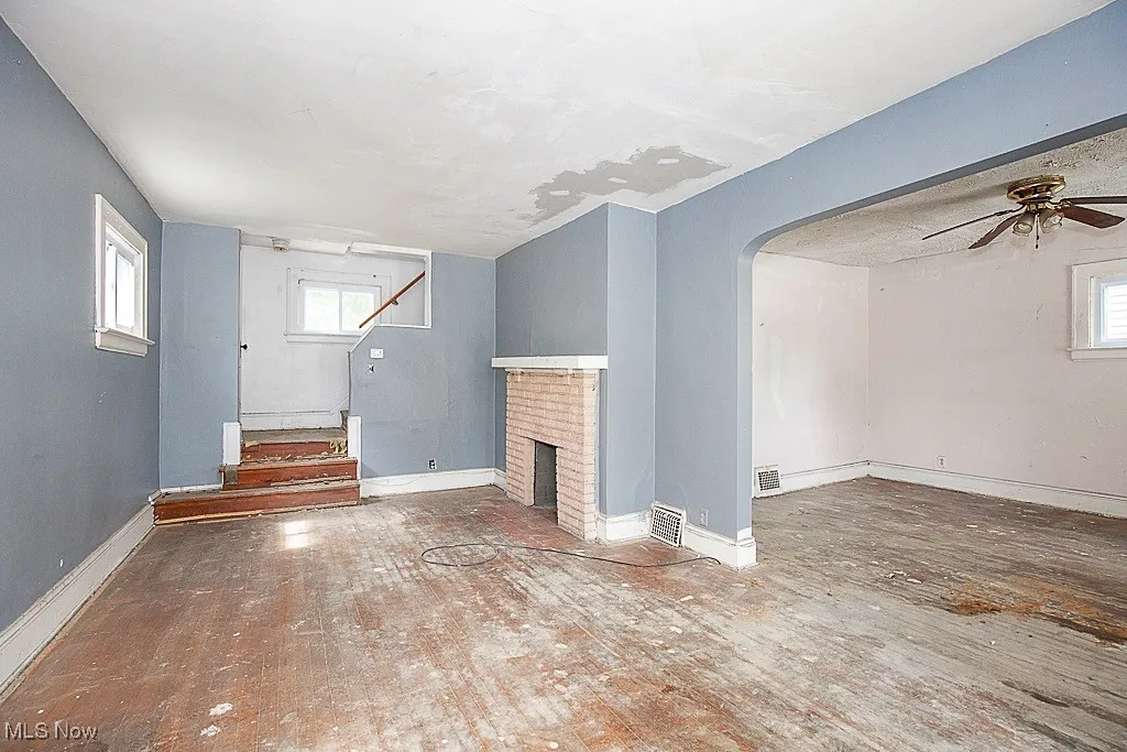 Unfurnished living room with hardwood / wood-style flooring, ceiling fan, arched walkways, stairway, and a brick fireplace