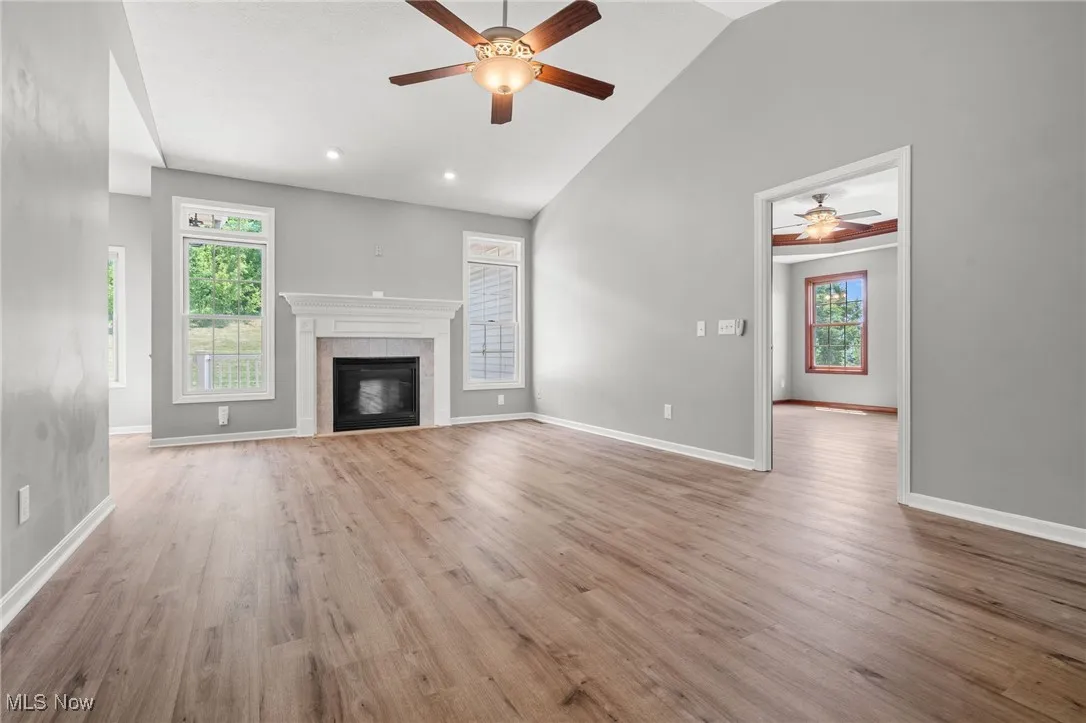 Unfurnished living room with a ceiling fan, wood finished floors, a tile fireplace, and high vaulted ceiling